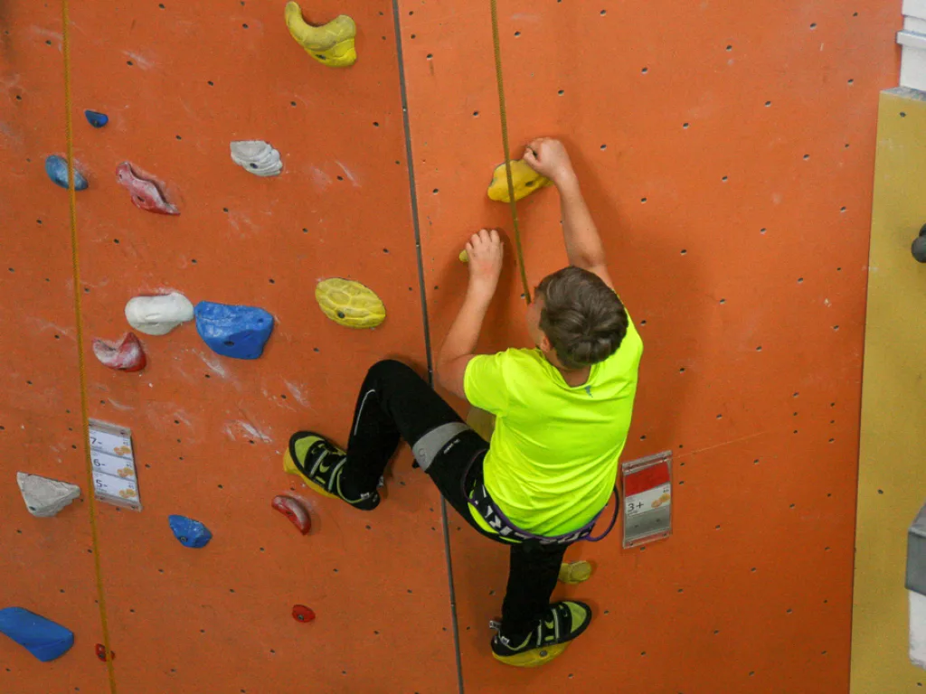 Person klettert eine orangefarbene Kletterwand hinauf.